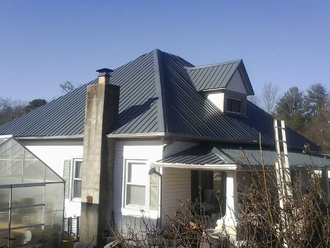 Dark blue standing seam metal roof on a white farmhouse with dormer — Slate & Tile Roof Repair by Roofing Brothers in Farmland
