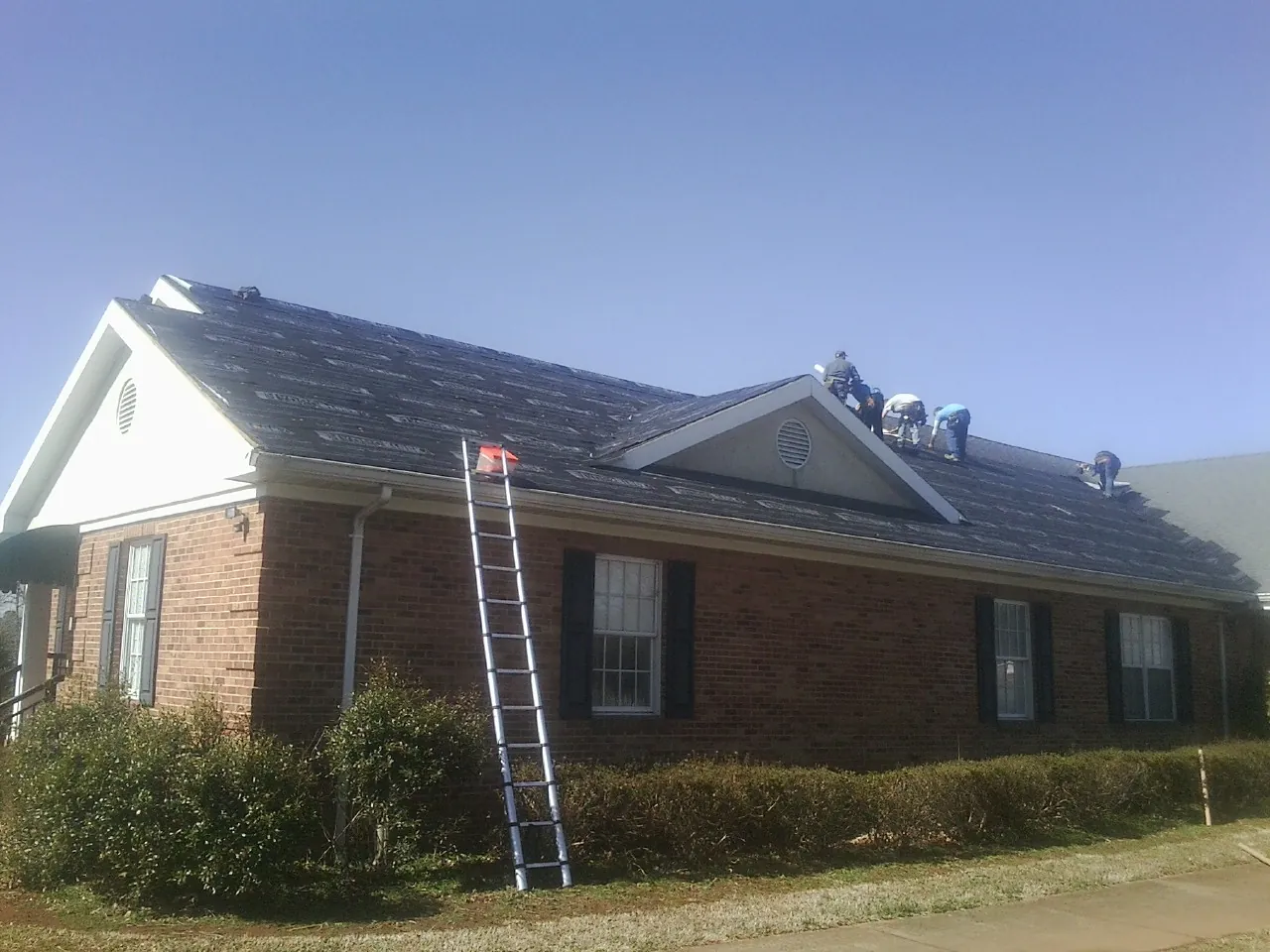 Crew tearing shingles off a brick ranch roof with a ladder set — Emergency Roof Repair work by our crew in Farmland