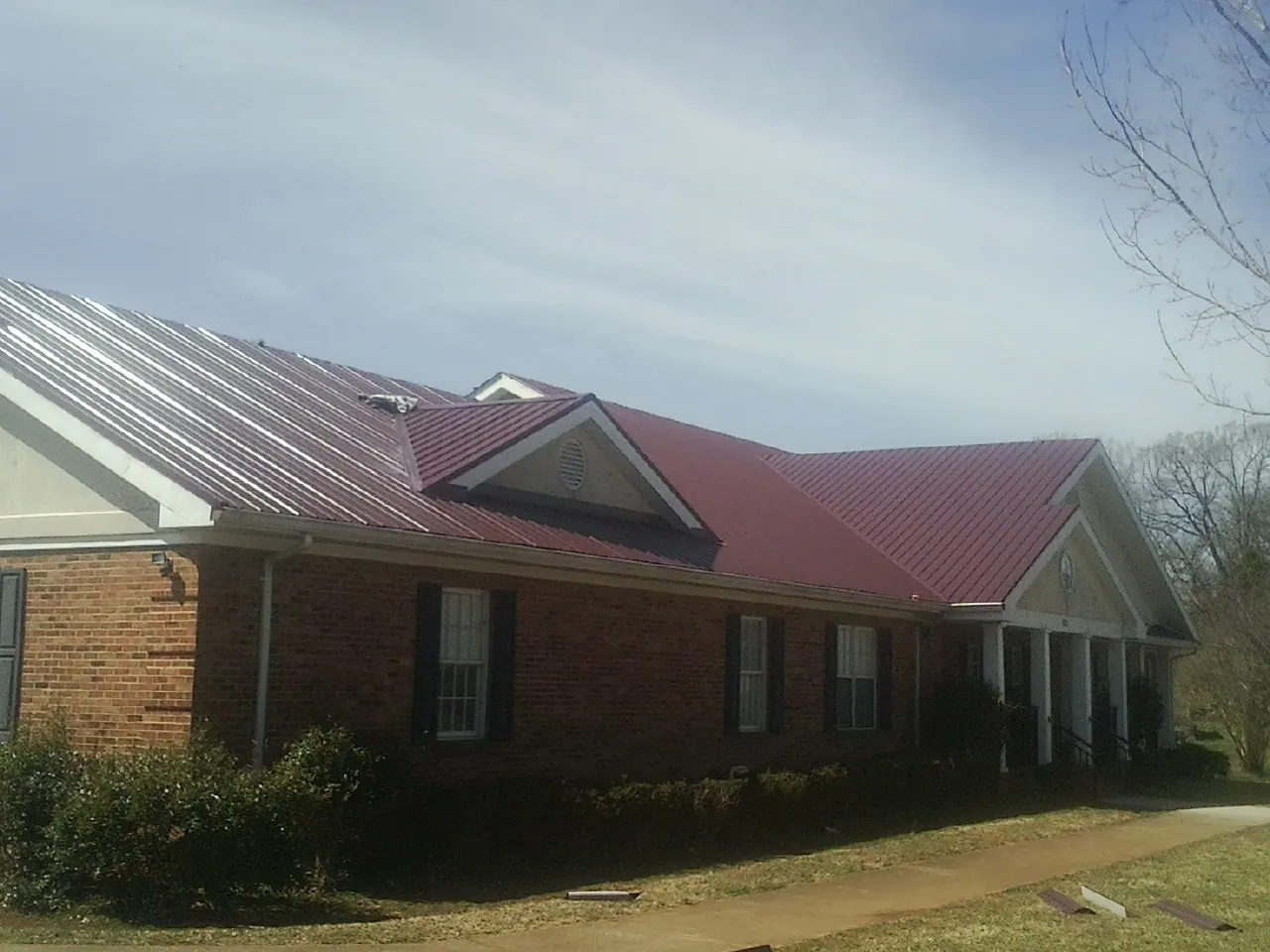 Red metal roof with gabled entries on a long brick building, from a Hail Damage Roof Repair job in Farmland
