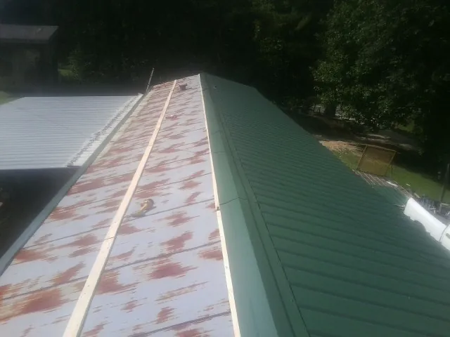 Old rusted panels beside newly installed green metal roofing — Wind Damage Roof Repair by Roofing Brothers in Farmland