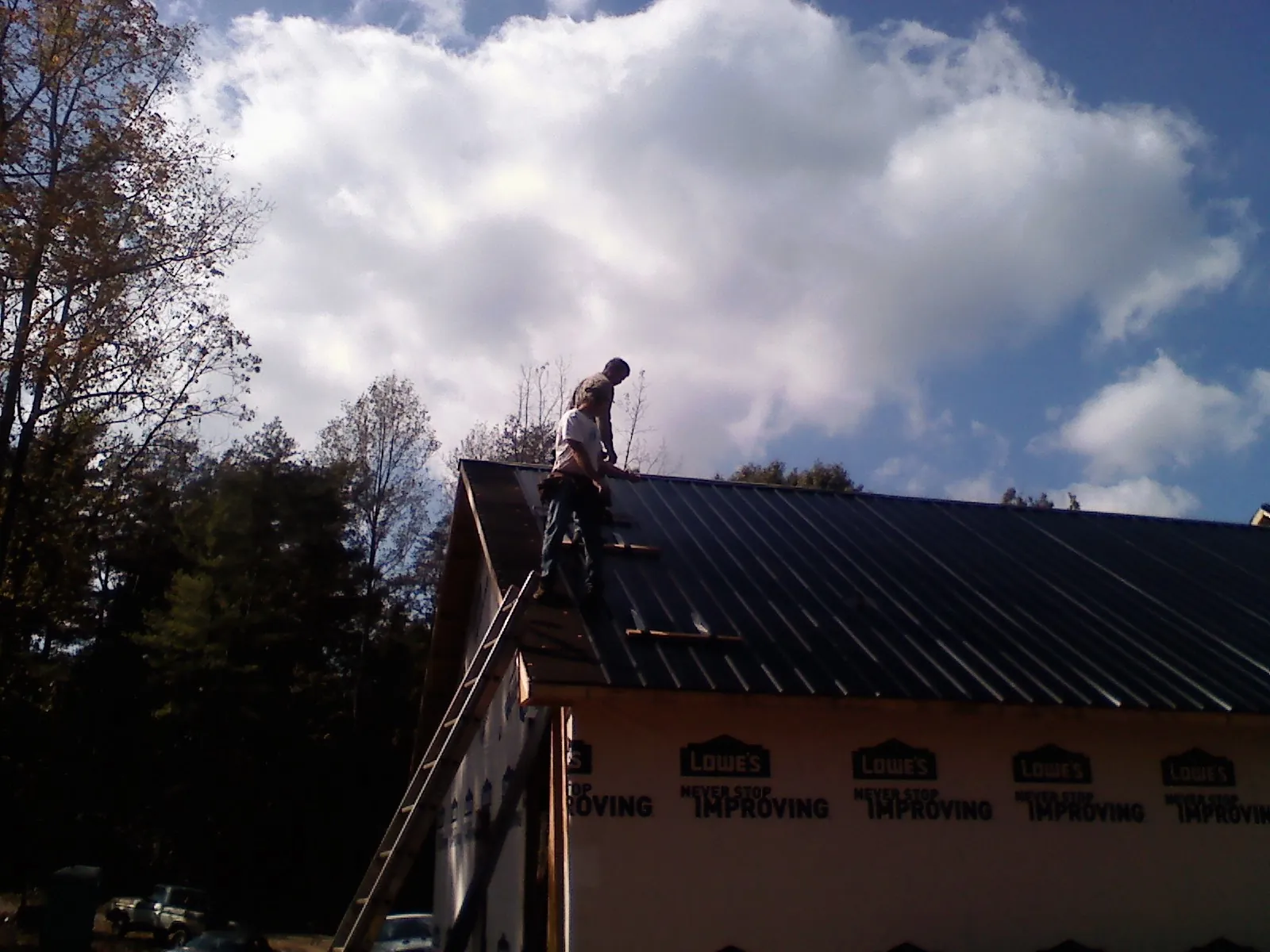 Roofer fastening dark metal panels high against a cloudy sky, from a Roof Inspection job in Farmland