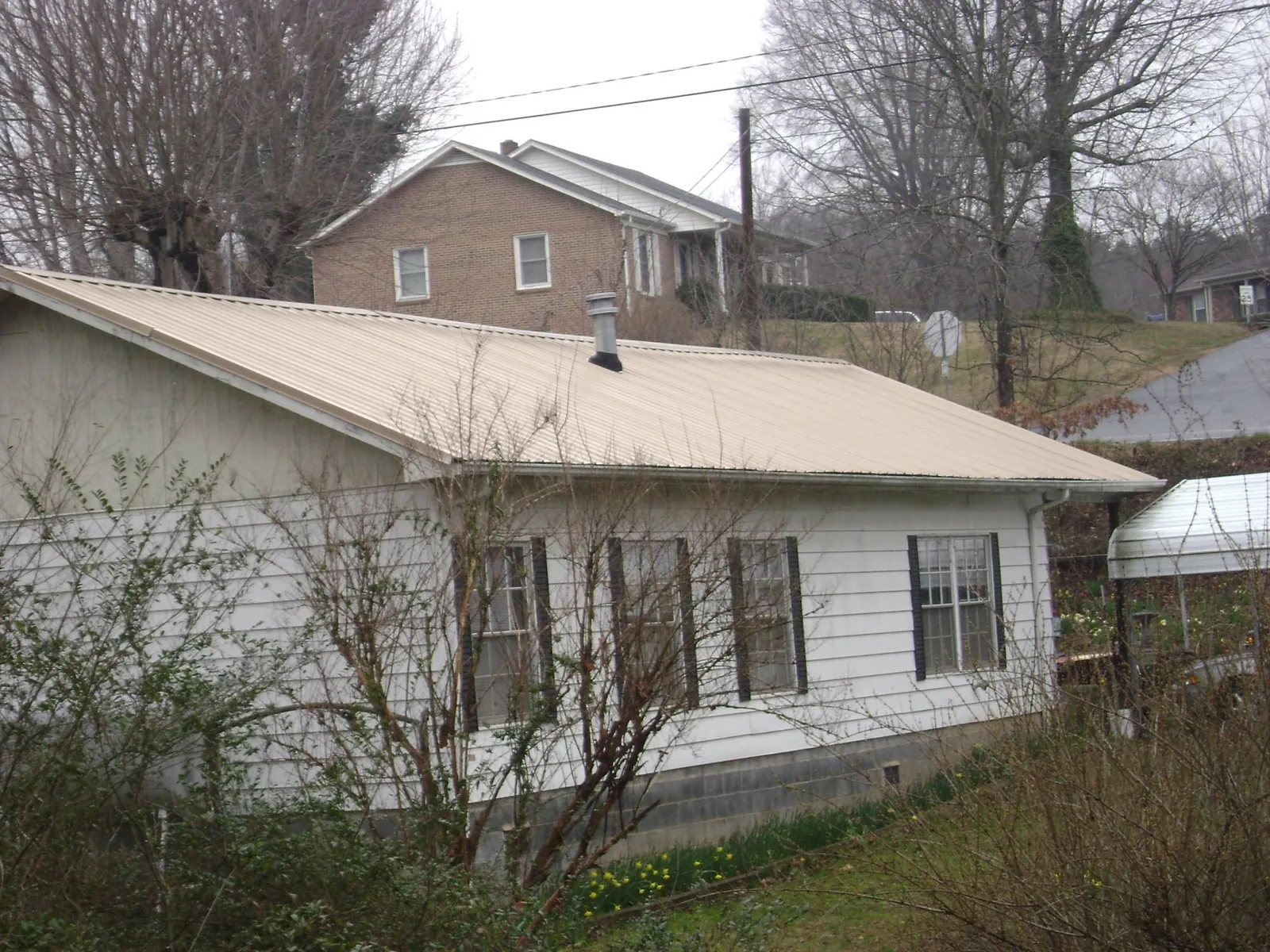 Tan metal roof on a white sided house set into a hillside — Commercial Roofing by Roofing Brothers in Farmland
