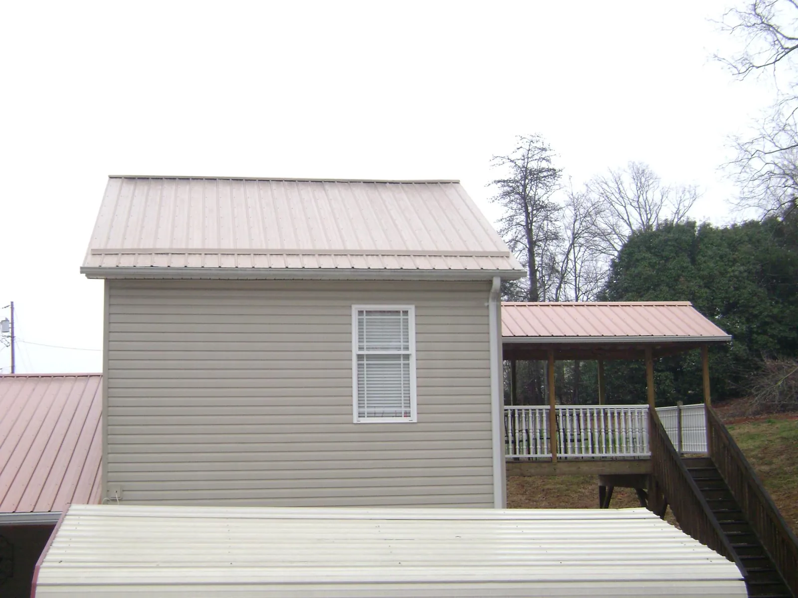 Tan metal roofs on a two story addition and attached porch, from a Roof Replacement job in Farmland