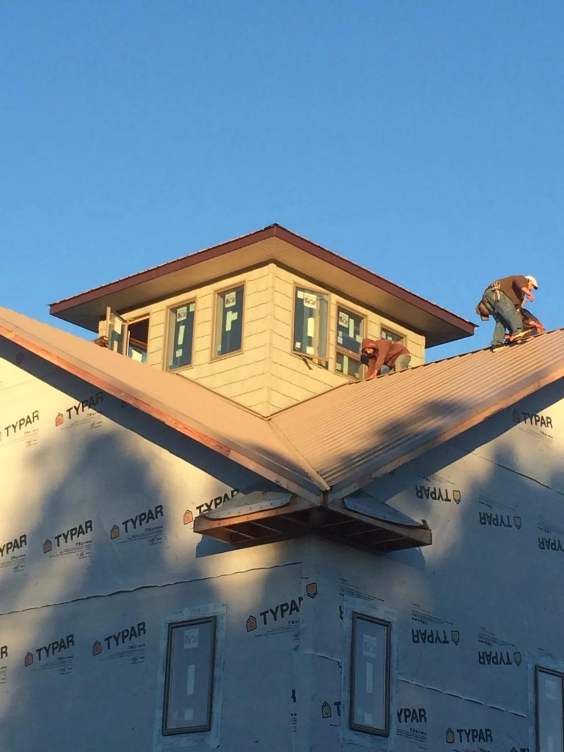 Roofers working around a rooftop cupola on a new metal roof at sunset — Roof Waterproofing in Farmland by Roofing Brothers